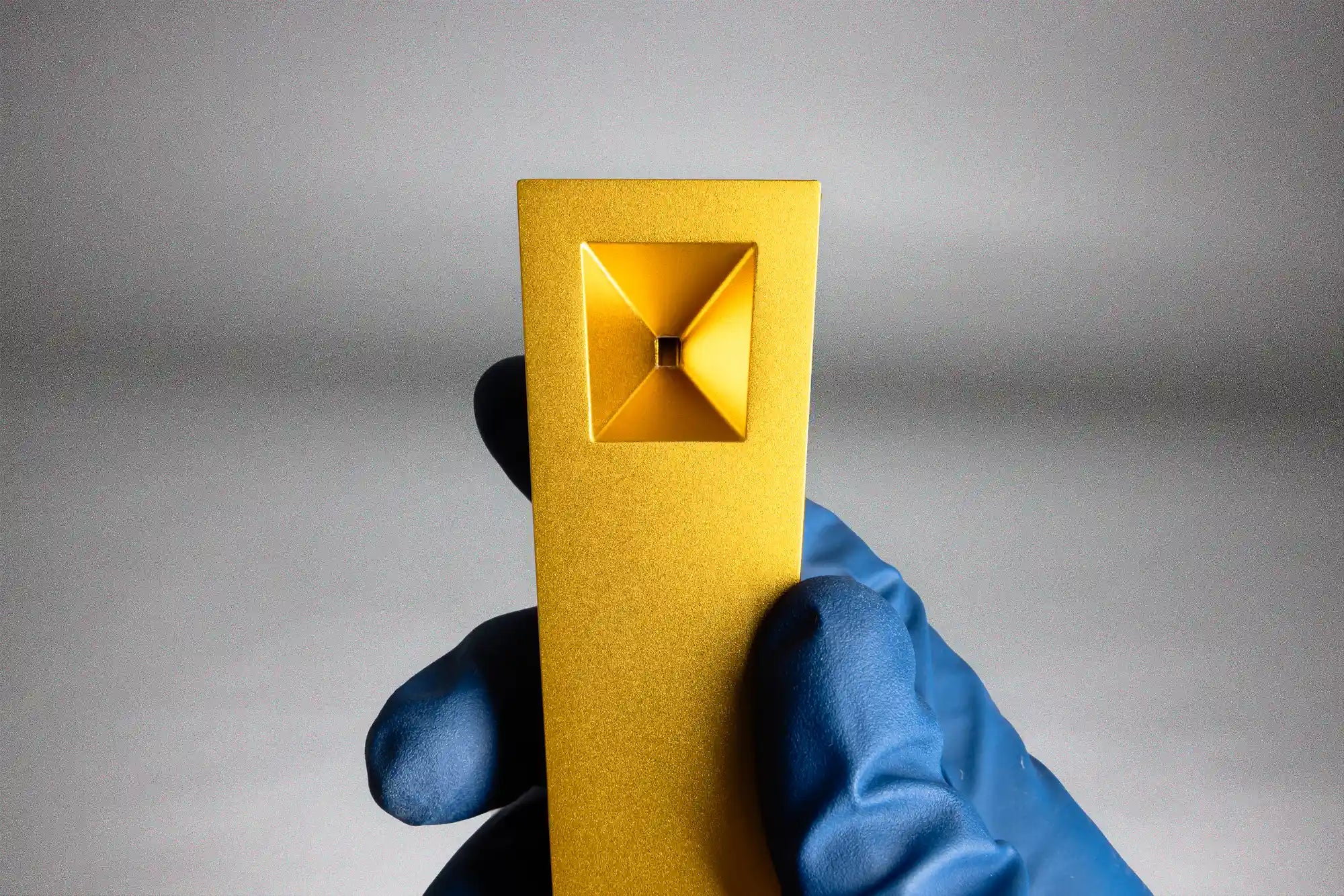 Tempest hand pipe in gold radiance held by a gloved hand against a gray background